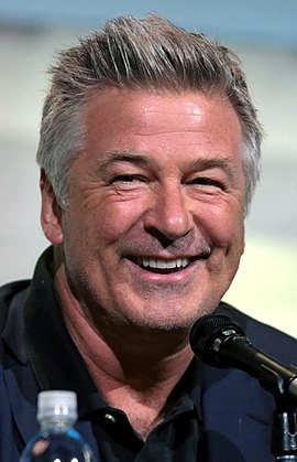 A man in his late fifties smiles while he is being photographed. He wears a dark tuxedo.