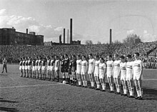 Photographie en noir et blanc de deux équipes de football alignées.