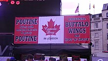 A poutine stand sign (also offering Buffalo wings, which originated In the United States) styled as the Flag of Canada during Canada Day celebrations in Trafalgar Square