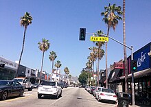 Fairfax Avenue with storefronts along both sides and traffic in the street