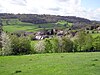 The roofs of houses and farm buildings in a green valley. Trees in the foreground