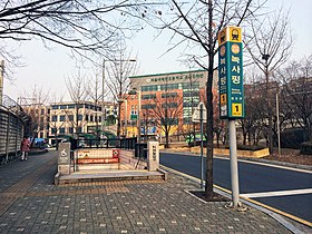 En ville, une rue et à gauche un trottoir avec une bouche de métro précédé d'un poteau indicateur du métro