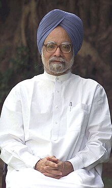 A portrait photograph of a bespectacled Indian man with a dark grey beard, 