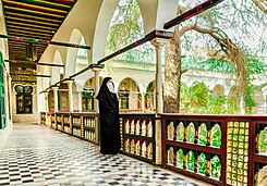 Veiled woman wearing a hijab looks out from a tiled balcony over orange trees in a central courtyard