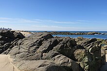 Granitic gneiss. The gneiss forms headlands and islets which submerge during high tide. It is a biologically rich environment with diverse habitats. Praia Quiao Pescador.jpg