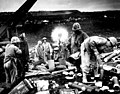 Across the litter on Iwo Jima's black sands, Marines of the 4th Division shell Japanese positions cleverly concealed back from the beaches. Here, a gun pumps a stream of shells into Jap positions inland on the tiny volcanic island. February 1945