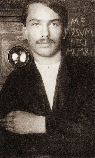 Photographie noir et blanc d'un jeune homme moustachu de face, en plan taille, l'air aimable, main gauche croisée sur le bras droit