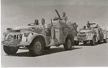 vehicles in convoy, each crewed by three men, in a desert terrain