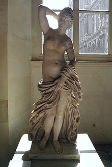 This is one of the many statues of the Greek Goddess Aphrodite. It is most likely a Roman copy of the Greek statue combining the “Aphrodite Anadyomene” type (in which the goddess is shown rising from the sea and adjusting her hair) and the “Aphrodite Pudica” type, in which she holds her drapery around her body, both created in the 3rd or 2nd century BC. The presence of different types of marble and the odd join at the bust and pelvis, visible from the back, may indicate that two separate statues were combined in the modern period.