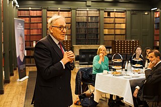 A man in a suit mid-speech in a grand library.