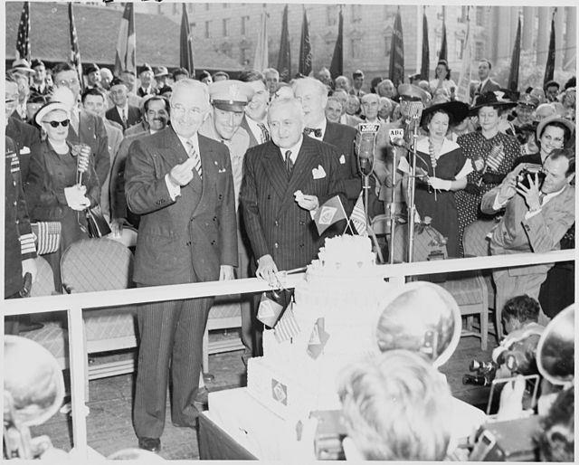 Presidents Dutra and Truman sampling a birthday cake decorated with Brazilian and U.S. flags.