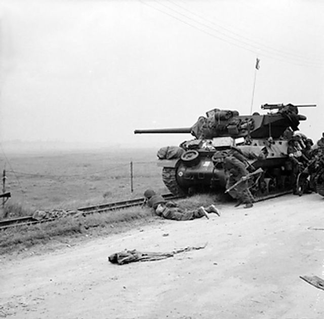 Troops take shelter near an M10 tank destroyer, used by 102nd (Northumberland Hussars) Anti-Tank Regiment; 6 June 1944