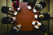 Photo prise à la verticale de huit personnes assises à une table octogonale, chacune sur un livre ouvert