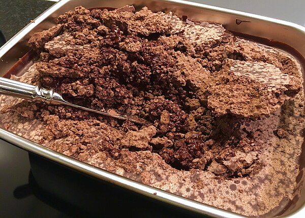 Untempered chocolate mass that has been left to cool at room temperature after conching, showing large cocoa butter crystals and a crumbly consistency