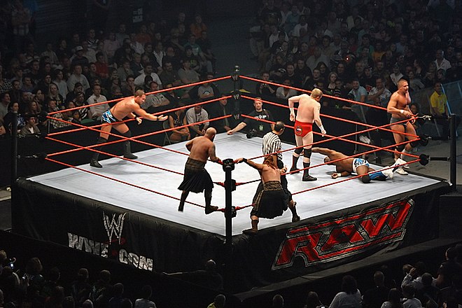 Action in a triple threat tag team match for the WWE World Tag Team Championship. Shelton Benjamin (on the mat) from The World's Greatest Tag Team has been isolated in the corner of champions Cade and Murdoch, well away from partner Charlie Haas; either of these teams can tag in the third team, The Highlanders.