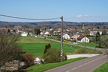 Kleurenfoto van een weg die door velden loopt.  Op de achtergrond: bebouwd gebied.