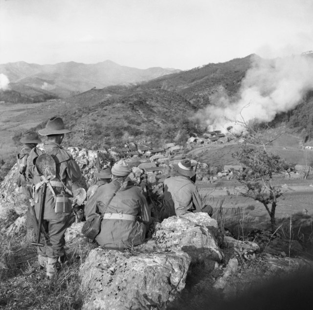 Troops from C Company, 3 RAR, watch for the enemy while a village in the valley below burns in November 1950