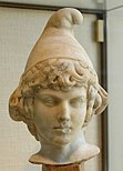 A marble bust of a curly-haired boy wearing an edgeless conical cap with the rounded peak bending forward