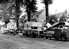 zwart en wit, tanks opgesteld aan de linkerkant van een straat;  soms reclame (merk sigaretten);  bomen langs de laan, winkels aan de zijkant;  onopvallende reclameslogans