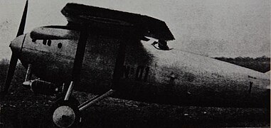 Photographie en noir et blanc d'un avion à hélice vu de côté, posé sur l'herbe.