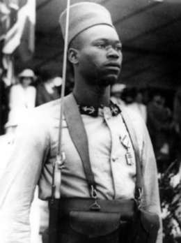 Foto di un soldato africano, giovane, in uniforme da schermagliatori, che mostra la Croce di Liberazione