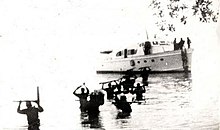 Cuban guerrillas holding rifles above their heads as they wade through the sea, having disembarked from a small boat