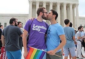 Two men kissing in front of the US Supreme Court. One is wearing a t-shirt with the words, Legalize Gay