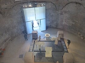 Vue intérieure du temple de Romulus, depuis la verrière située dans la basilique Santi Cosma e Damiano (ancien vestibule de la basilique). En 2015, le temple accueille la reconstruction du mobilier de la fontaine de Juturne (Fons Iuturnae).
