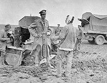 Um oficial da Divisão de Blindados Russa falando com um soldado russo ferido, enquanto que atrás deles os outros soldados tentam retirar um Lanchester atolado na lama; esta imagem foi tirada durante a retirada da Ofensiva de Kerensky no verão de 1917 na Galícia (porção austro-húngara da Polónia).