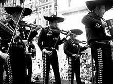 Fotografia que mostra um grupo de músicos mexicanos vestidos com trajes tradicionais e sombreros.