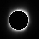 A black circle outlined in hazy streaks of white emanating from the circle to the edges of the image all on a solid black background