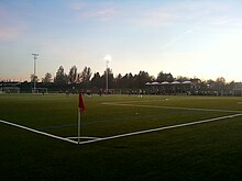 Césped de fútbol, ​​con varias personas jugando al fútbol al final del día.