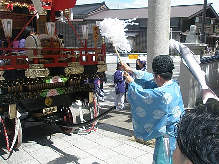A priest purifies the area in front of the residence of a kami.