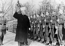 a male dressed in robes reviewing a parade of soldiers