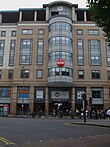 A beige building with a circular, red sign in the middle stating "Coca-Cola" in white letters and a rectangular, blue sign below