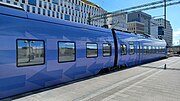 Pågatåg på Hyllie station med nybyggda hus vid Skrivaregatan i bakgrunden.