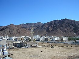 Black mountains in a desert with a white mosque with a minaret in the foreground