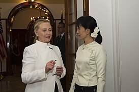 Хилари Клинтон 2011. године стоји са бурманском (мјанмарском) демократском лидерком Аун Сан Су Ћи, с којом разговара о демократским реформама у тадашњој Бурми које су спровођене у раздобљу од 2011. до 2015. године; обе даме су обучене у бело и имају реп, а Клинтонова је на левој страни слике
