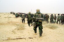 US Marines escort captured enemy prisoners to a holding area in the desert of Iraq on 21 March 2003. U.S. Marines with Iraqi POWs - March 21, 2003.jpg