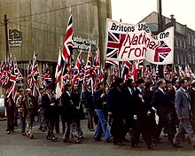 Photograph of people carrying Union Flags, demonstrating outside a factory.