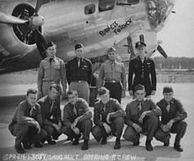 The nose of a propeller airplane with the name Fearless Fosdick painted on it. Four officers are standing; six enlisted men are kneeling in front.