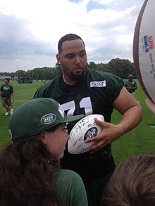 Ein American-Football-Spieler signiert einen weißen Ball vor den Fans.