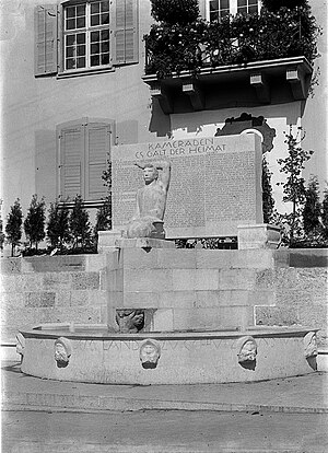 Das Wehrmannsdenkmal in seiner Ursprünglichen Fassung, wo die Urne von Jakob Probst in die Mauer eingelassen ist. Zum Andenken für die im Militärdienst stehenden Grippe- und Unfalltoten aus der Baseler Landschaft (Spanische Grippe-Epidemie 1918). Das Denkmal musste 1934 überarbeitet werden. Aus der Skulptur wurde ein Eichenblattzweig? herausgemeisselt und anstelle des offene Buch auf seinen Knien, ein Helm darauf gesetzt. Damit war die sakrale Symbolik des Werks zerstört.