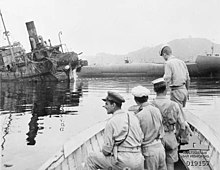 Vue en noir et blanc de l'avant d'une barque avec 4 soldats. En arrière-plan un navire naufragé.