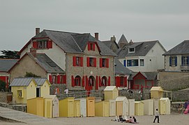Vue d’une maison aux volets rouges derrière une rangée de cabines jaunes.