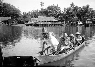 Bewoners peddelen een boot over de rivier naar het dorp Tallo (1920)