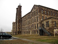 Large old four-story building that is gray-brown with double chimney on left