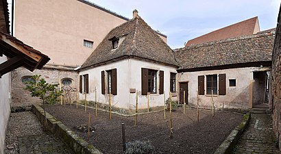 Kleurenfoto van een klein huis en een kleine tuin omgeven door hoge muren.