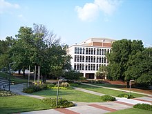 A sidewalk surrounded by landscaped green space in the foreground with a four-story white concrete building in the background.