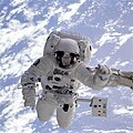 Астронавтът Майкъл Гернхарт, захванат от „ръката“ на совалката на фона на Земята.